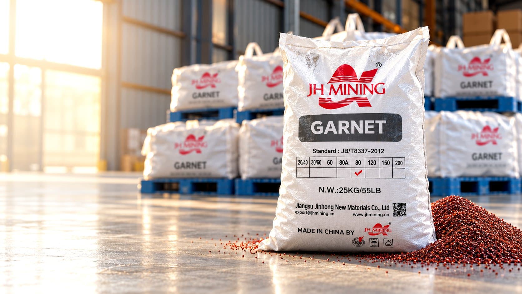 A 25 kg bag of garnet abrasive beside a pile of red granules in a sunlit warehouse